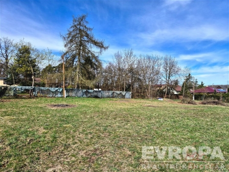 Pozemek s travnat�m povrchem, vhodn� pro stavbu, obklopen� stromy a ke�i, nab�z� klidnou lokalitu s venkovskou atmosf�rou.