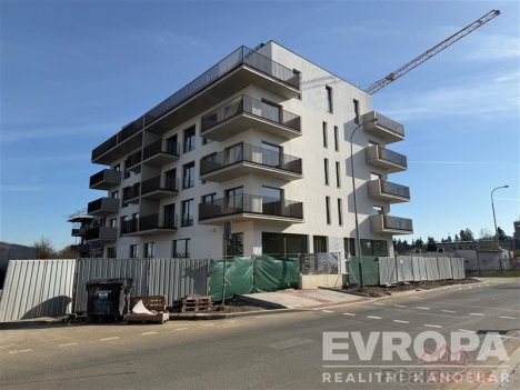 Novostavba bytov�ho domu s modern� architekturou a balkony, b�l� fas�da, nach�z� se na rohu ulice.