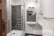 Mal� koupelna s modern� sprchou, obklady z tmav� dla�by a z�v�sn�m umyvadlem. ��eln� uspo��d�n� prostoru a sv�tl� st�ny.