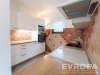 Modern� kuchy� s d�ev�nou pracovn� deskou, keramick�mi dla�dicemi a vestav�nou troubou, sv�tl� prostor s oknem.