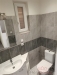 Mal� koupelna s modern� dla�bou v �ed�m t�nu, keramick� umyvadlo s b�lou sk���kou a okno pro p�irozen� osv�tlen�.