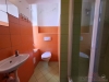 Mal� koupelna s oran�ov�mi dla�dicemi, sprchov�m koutem a b�l�m umyvadlem, modern� design, sv�tl� obklady a kompaktn� uspo��d�n�.