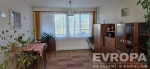 Sv�tl� ob�vac� pokoj s parketovou podlahou a velk�mi okny, vybaven� d�ev�n�m n�bytkem v retro stylu.