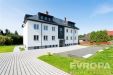 Praktick� exteri�r bytov�ho domu s modern� fas�dou, upravenou zahradou a dl�d�n�m parkovac�m prostorem, ide�ln� pro rodinn� bydlen�.