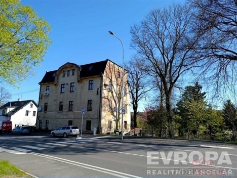 Star�� bytov� d�m s historickou fas�dou, nach�zej�c� se na rohu ru�n� ulice, obklopen� vzrostl�mi stromy a s parkovac�mi m�sty v okol�.