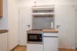 Kompaktn� modern� kuchy� s vestav�nou mikrovlnnou troubou, sv�tl� d�ev�n� pracovn� deska, parketov� podlaha, sv�tle �ed� obklad na st�n�.