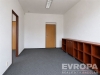 Pr�zdn� pokoj s kobercovou podlahou, d�ev�n� police, b�l� st�ny, modern� osv�tlen�.