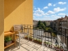 Balkon s dla�bou, kter� nab�z� v�hled na m�stskou krajinu, s pohodln�m d�ev�n�m posezen�m a kv�tinov�mi truhl�ky pro p��jemn� venkovn� posezen�.