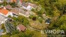 Pohled na rozlehl� pozemek s udr�ovanou zahradou, obklopen� vzrostl�mi stromy a pobl�� rodinn�ch dom�, ide�ln� pro stavbu nebo rekrea�n� ��ely.