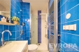 Modern� koupelna s modrou dla�bou, sprchov�m koutem a b�lou sanitou. Sv�tl� prostor obsahuje designov� �eb��kov� radi�tor a elegantn� umyvadlo.