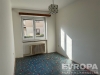 Pr�zdn� pokoj s velk�mi okny, kter�mi pronik� sv�tlo, m� star�� koberec a topen� pod oknem, ide�ln� pro rekonstrukci nebo modernizaci.